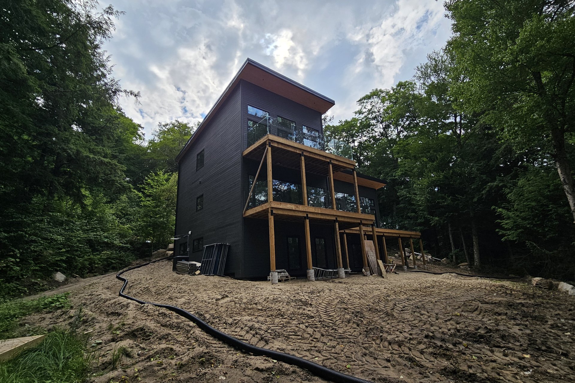 Exterior — Dark Siding & Detail A modern, multi-story house with dark siding and multiple balconies with glass railings, nestled among trees on a sloped landscape.