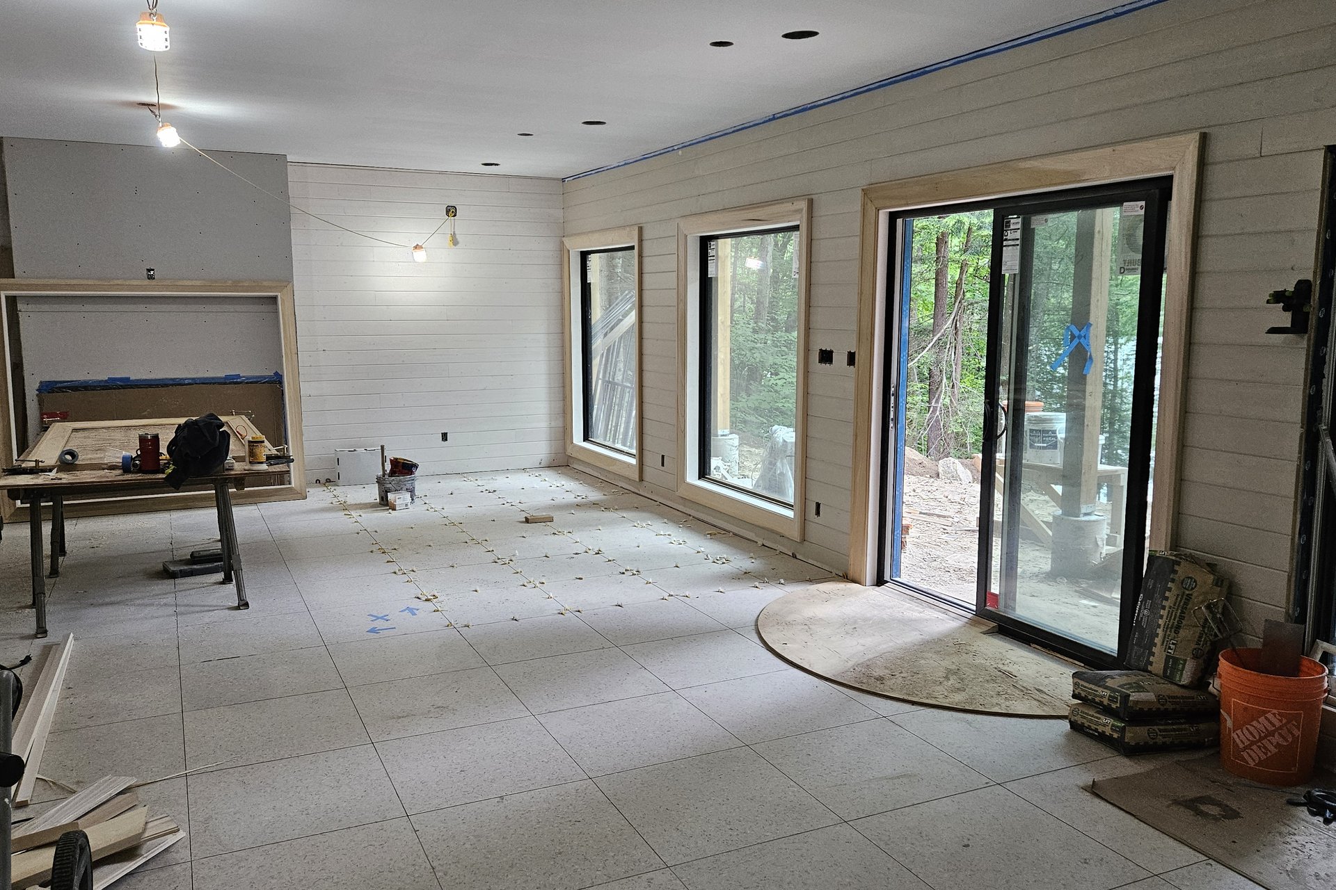 Interior — Feature Wall A wide interior shot of a room under construction with white shiplap walls, multiple windows and a sliding door, and various tools on the floor.