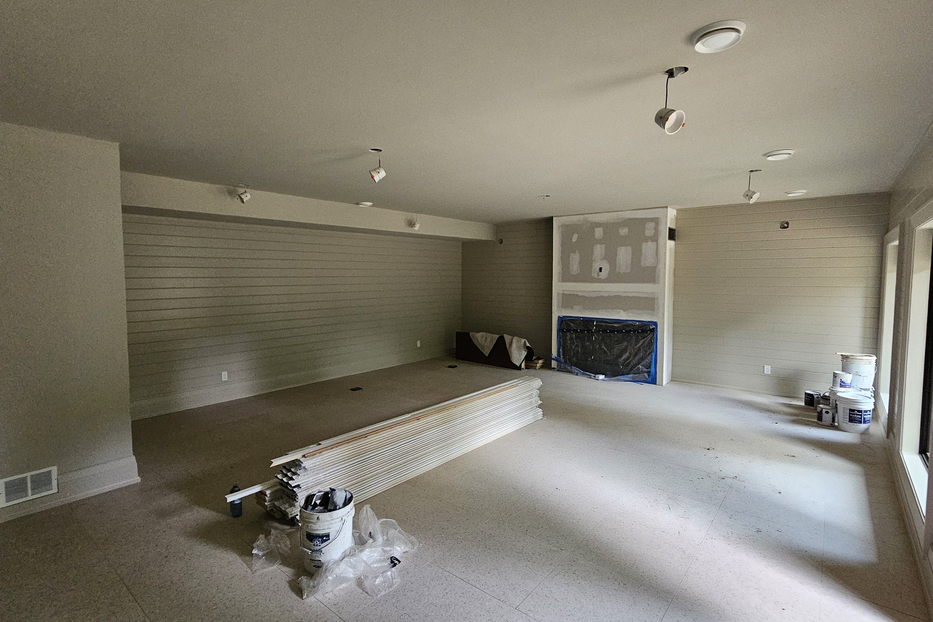 Basement — Finished Space A spacious basement room with light-colored walls, recessed lighting, and a partially constructed fireplace, with building materials on the floor.