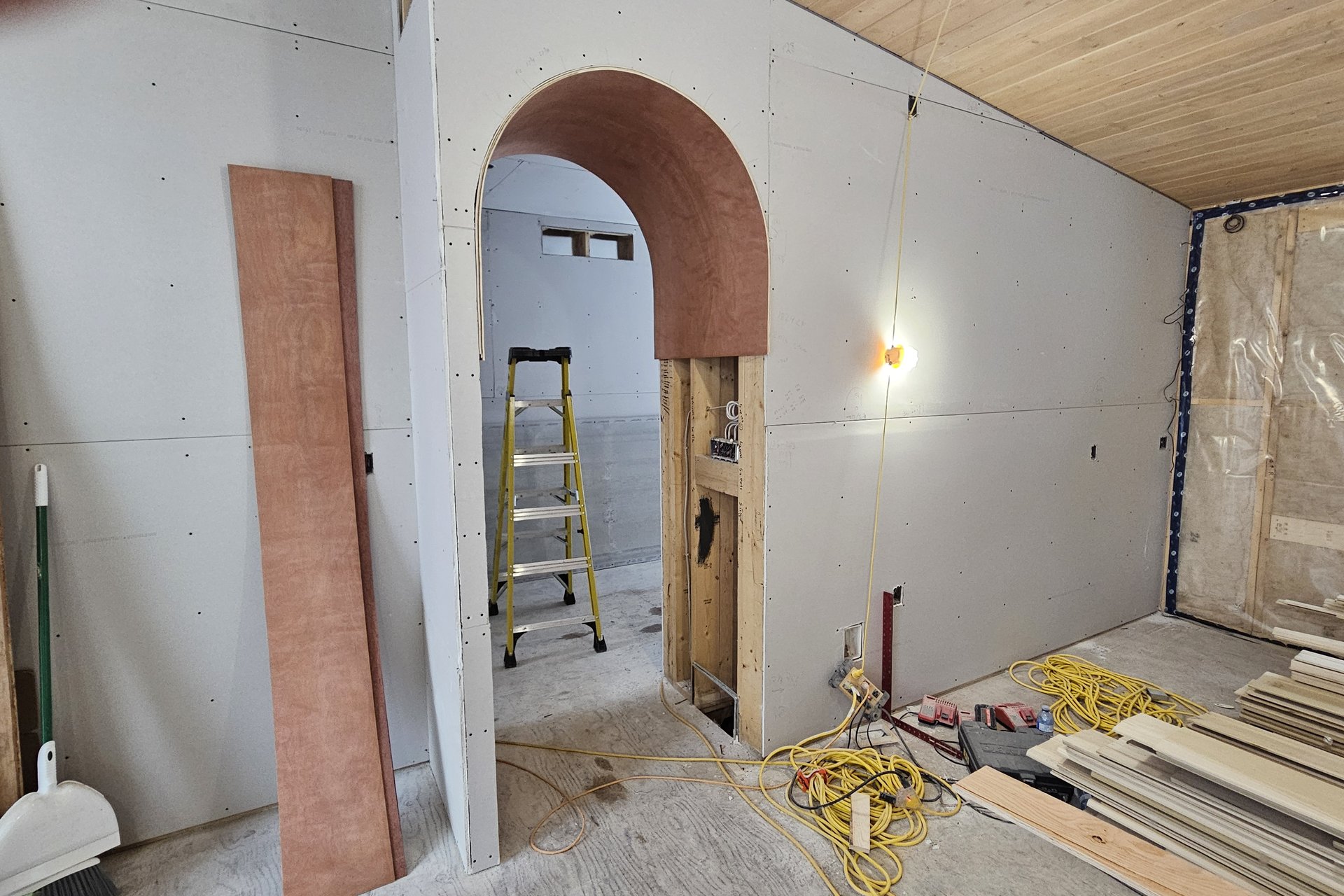 Interior — Door Installation An interior shot of a room under construction with an arched doorway and exposed wooden ceiling, demonstrating the early stages of finishing.