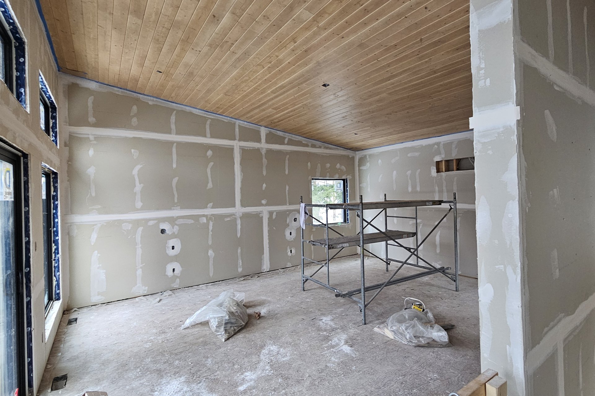 Interior — Finishing An interior room with finished drywall joints ready for paint, a wooden slatted ceiling, and scaffolding in the center, indicating ongoing construction.
