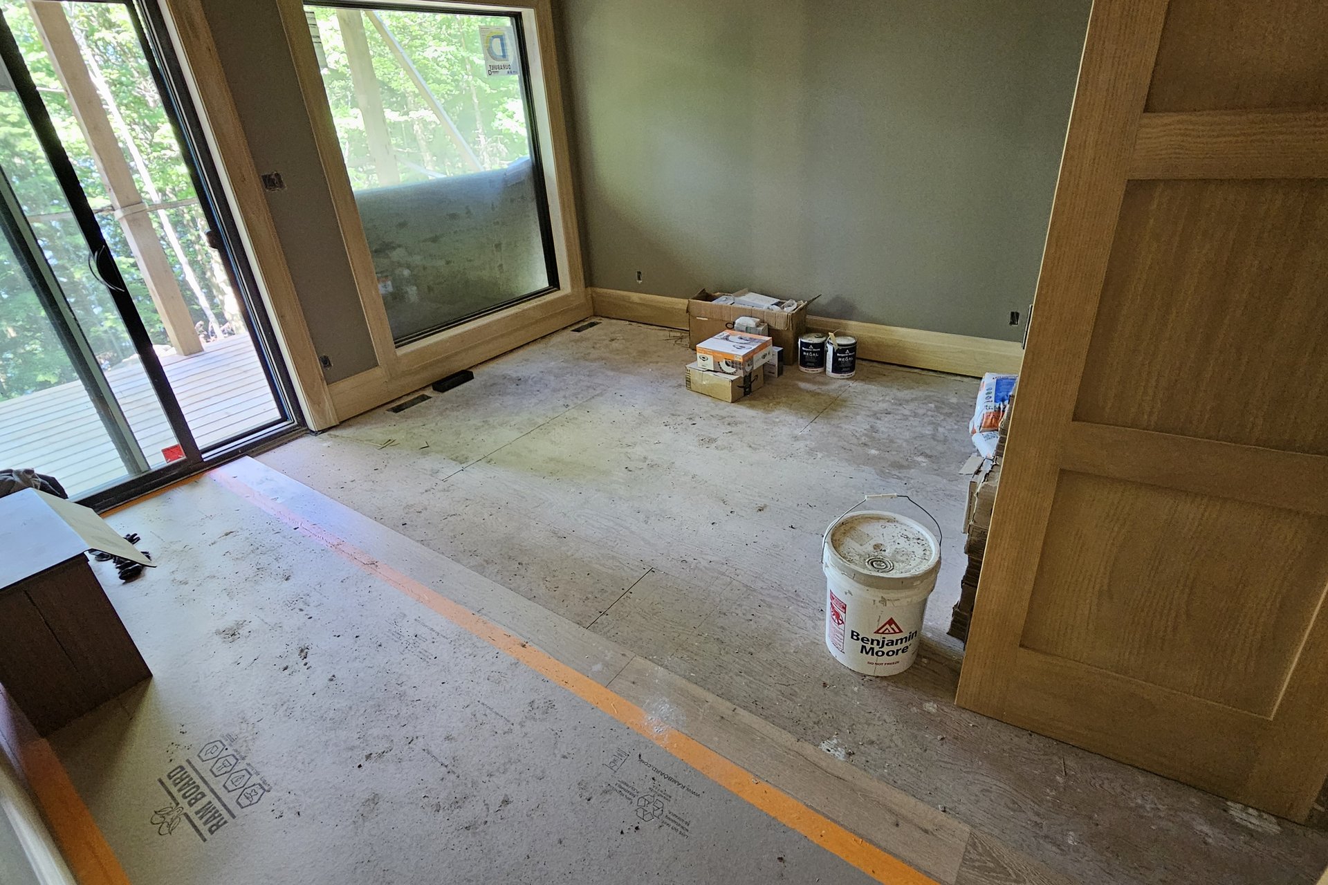 Interior — Door Installation An interior room, possibly a bedroom or office, is undergoing finishing with a wood door, large window, and building materials on the floor.