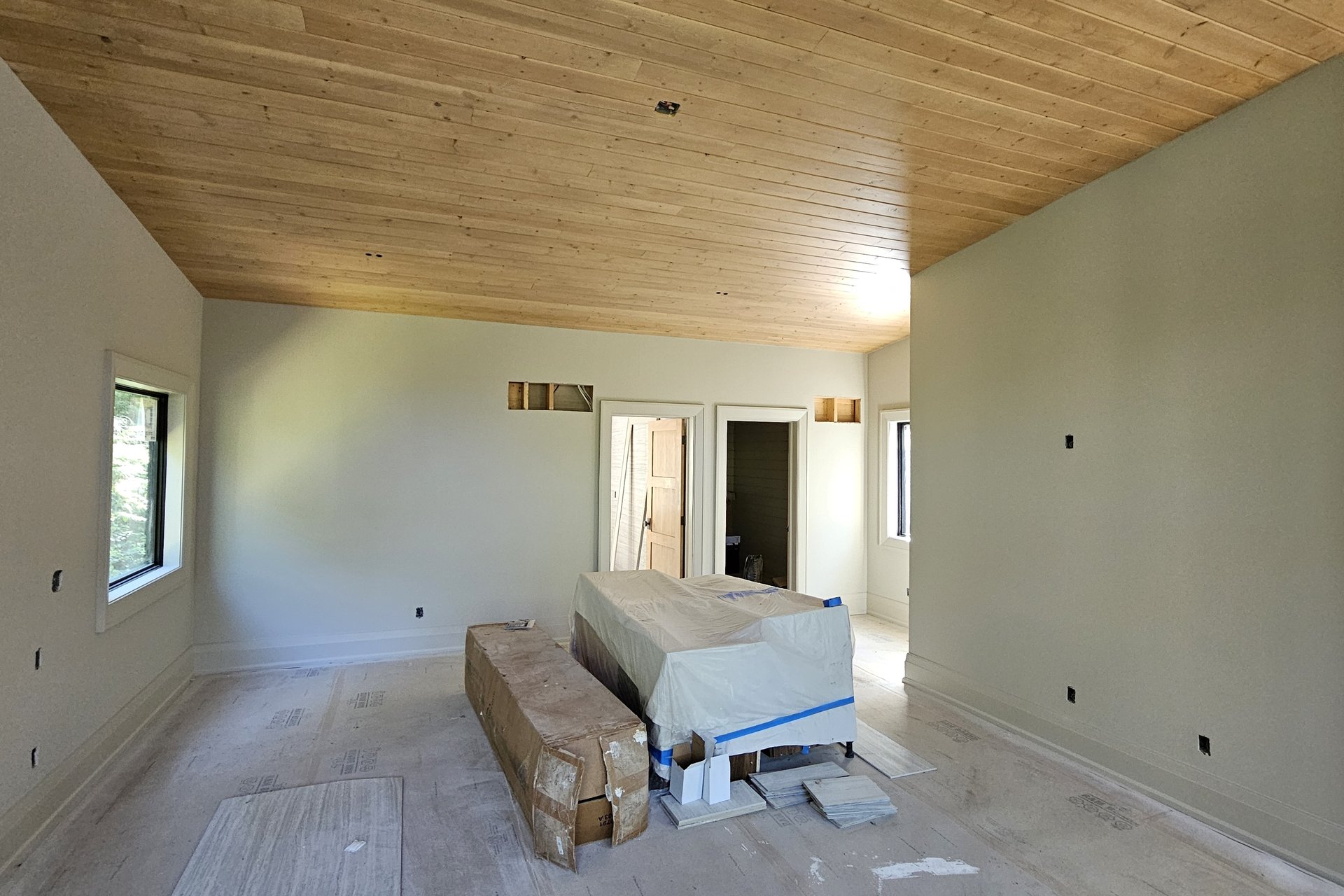 Interior — Door Installation An interior room under construction with a finished wooden ceiling and light-colored walls, featuring a large covered item in the center and doorways in the background.