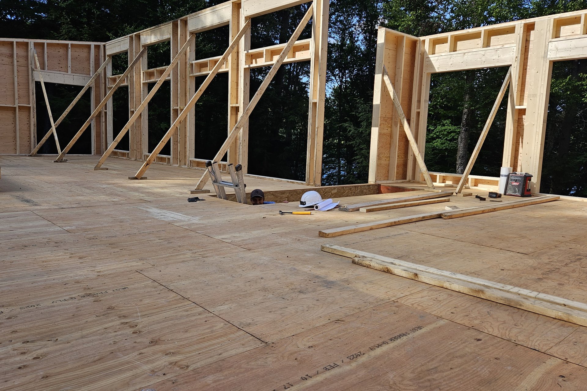Construction — Framing Stage Framed walls with large openings are visible on a wooden floor, indicating the early stages of building construction, with a body of water in the background.