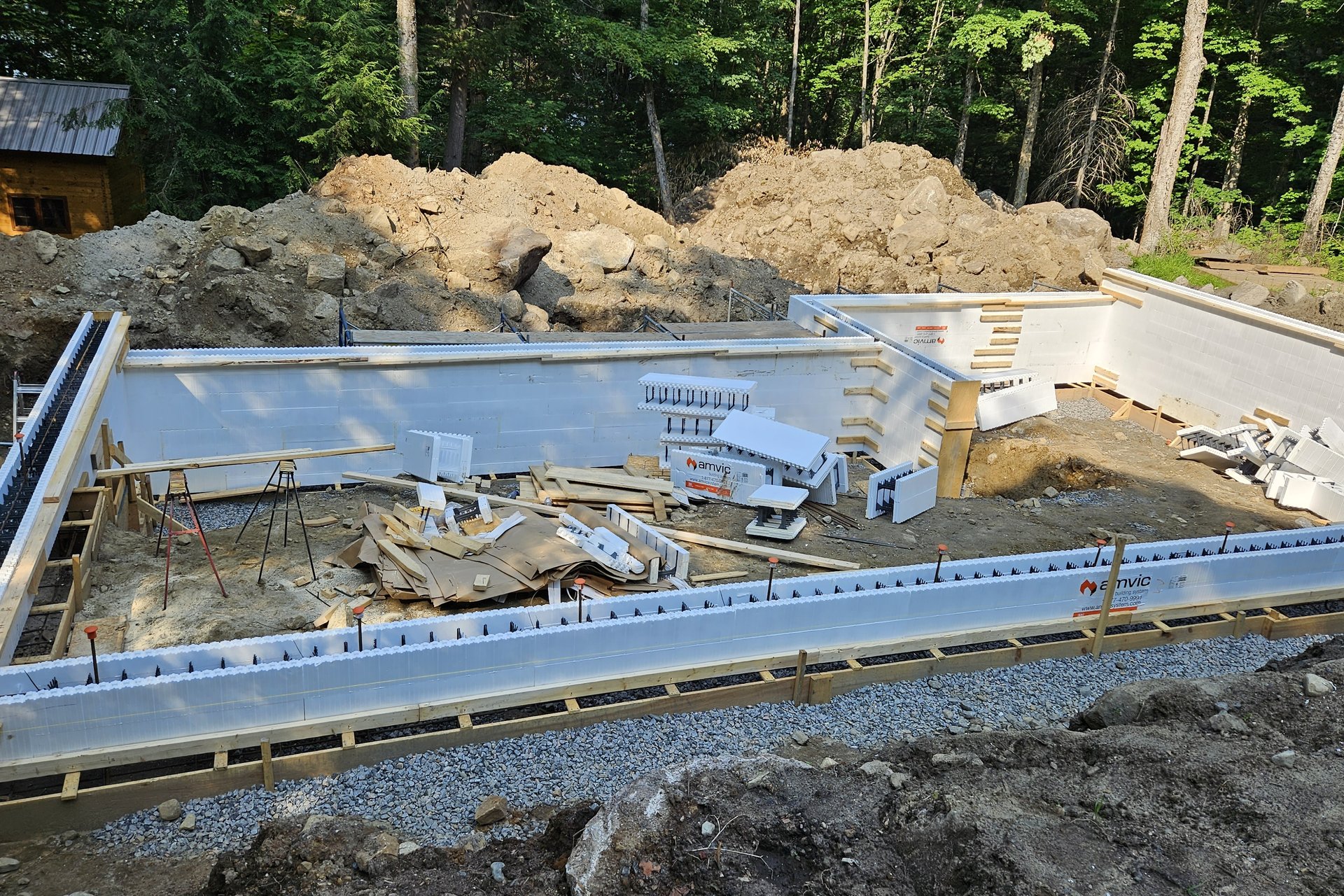 Foundation — Aerial View An aerial view of a construction site showing the concrete foundation and formwork laid out for a new building, with piles of dirt and trees in the background.