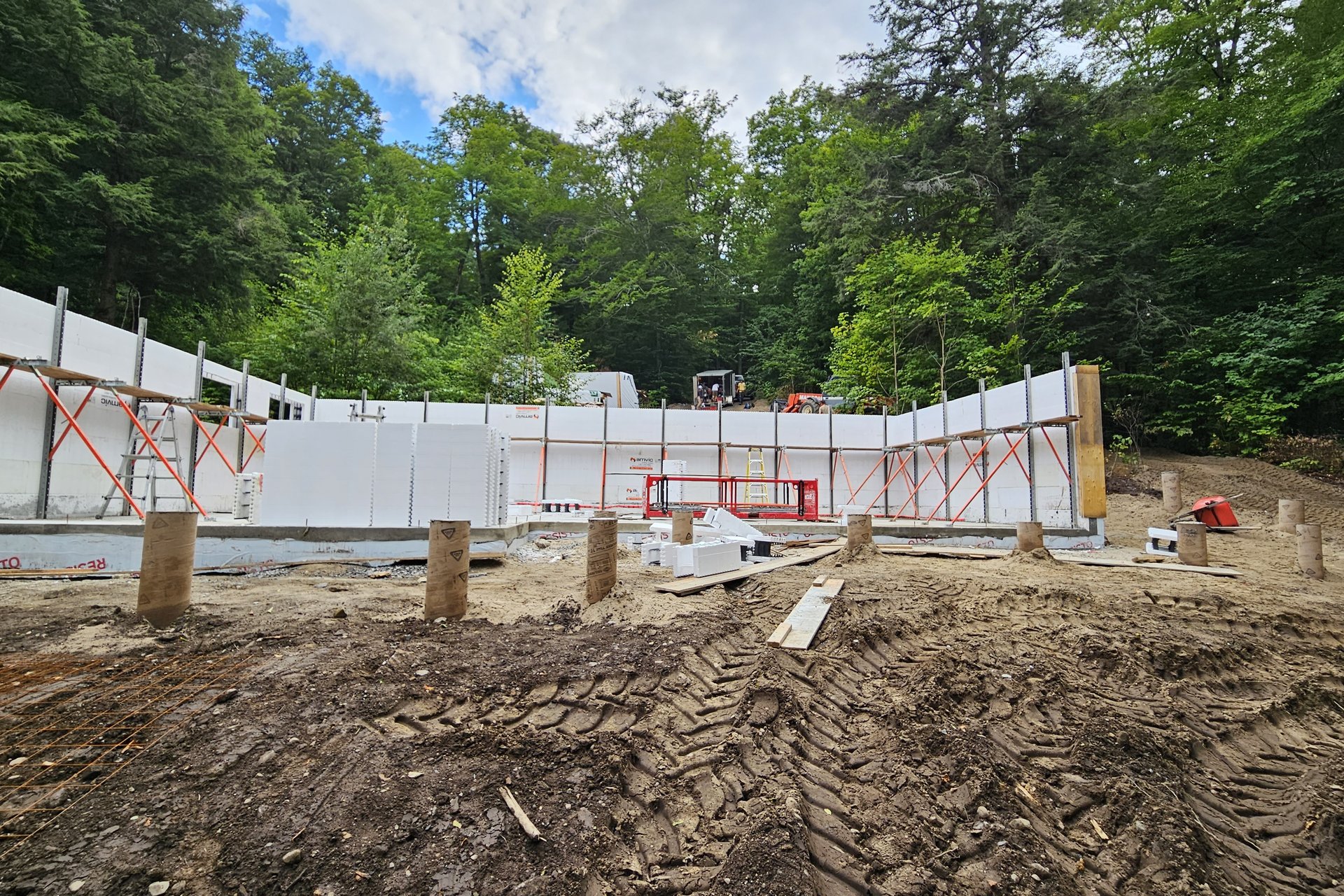 Foundation — Formwork An outdoor shot of a building foundation under construction, with white insulated concrete form (ICF) walls rising from the ground, surrounded by cleared earth and trees.